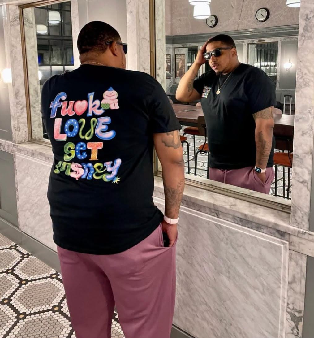 Sinatris wearing a WEWORKINGWYD shirt in front of a mirror