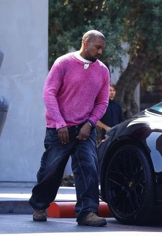 Ye wearing a bright pink sweater, dark jeans and boots